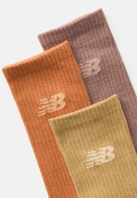 Três pares de meias caneladas nas cores laranja, roxo e amarelo, apresentando um discreto logótipo "NB" numa tonalidade mais clara em cada uma.