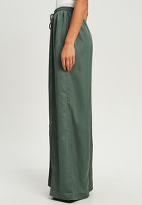 Groene, lichtgewicht, wijdvallende broek met een koordsluiting in de taille, voorzien van een soepele textuur en zijsplitten voor bewegingsgemak.
