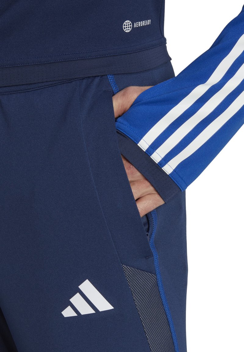 Navy sportjack met witte strepen op de mouwen, zachte textuur, slim fit, met ritszakken en een wit logo op de borst.
