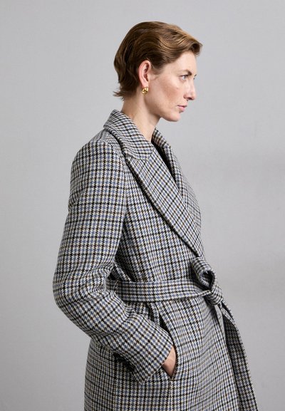 Long belted coat in a houndstooth pattern with blue and beige tones. Features wide lapels, side pockets, and a textured fabric.