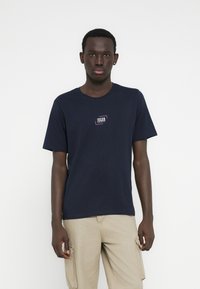 Camiseta de algodón azul marino con mangas cortas y cuello redondo, con un pequeño logo impreso en el pecho. Diseño liso, sin patrones.