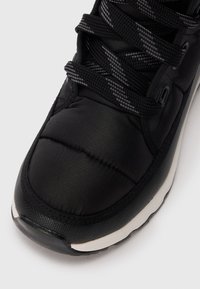 Black athletic shoe with a padded upper, textured laces, and a white rubber sole; features a smooth, sleek finish with stitching details.