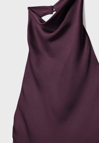Robe violette sans manches avec un col haut et deux boutons recouverts de tissu sur l'épaule.