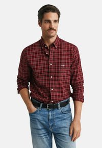 Red and black plaid button-up shirt with a pointed collar, long sleeves, and white buttons, worn with light blue denim jeans and a black belt.