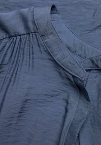 Mørkeblå stofbluse med en tekstureret, krøllet finish. Har en rund halsudskæring og samlede detaljer ved skuldersømmen.