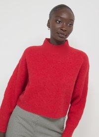 Roter, gestrickter Pullover mit einem hohen, gerippten Kragen und strukturiertem Muster. Mit überschnittenen Schultern und lockerer Passform. Kombiniert mit karierter Hose.