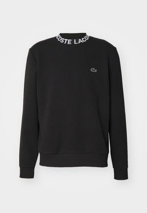 Fekete kapucnis pulóver hosszú ujjakkal, bordázott mandzsettákkal és bordázott gallérral, amelyen a "LACOSTE" márkajelzés található. Kicsi Lacoste logó az elején.