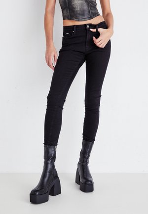 Pantalones vaqueros skinny negros de denim, con cintura alta, bolsillos frontales y ajuste slim. Combinados con elegantes botas negras de tacón alto.