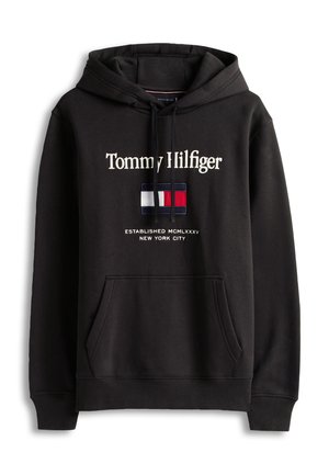 Melns džemperis ar kapuci, uz kura izšūts teksts "Tommy Hilfiger" baltā krāsā, kā arī sarkana, balta un zila logotipa plāksteris. Aprīkots ar kenguru kabatu un auklām.