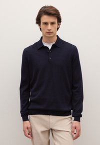 Marineblauwe pullover met lange mouwen, kraag met drie knopen, gebreide textuur, gecombineerd met lichtbeige broek. Eenvoudig en strak ontwerp.