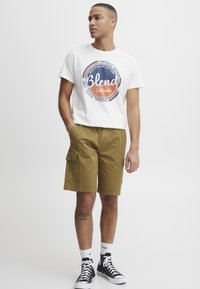 Hvit bomulls T-skjorte med en fargerik "Blend California" grafikk, kombinert med khaki cargo-shorts med sidelommer og rett ben.