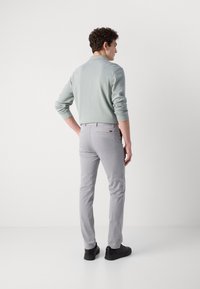 Light green knitted sweater with ribbed texture, paired with light gray fitted pants. Solid color, featuring a back pocket detail. Black shoes.