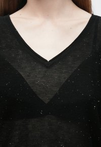 Črna top majica z v-izrezom iz prosojne tkanine z nežnim vzorcem bleščic, ima sproščen kroj in teksturiran izrez na vratu.