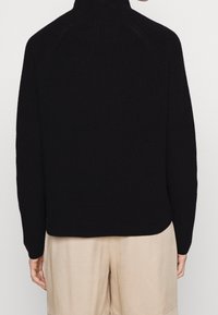 Schwarzer Strickpullover mit hohem Kragen, Raglanärmel und lässiger Passform, ausgestattet mit gerippter Textur und abgerundetem Saum.