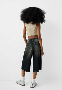 Klippekantet beige denimtop, mørkevidde jeans med flossede kanter, baglommer og sølv sneakers med hvide sokker.