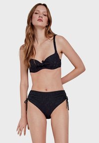 Ensemble de bikini noir avec un design texturé, comprenant un haut noué et un bas taille haute. Comprend des liens latéraux ajustables et des bretelles douces.