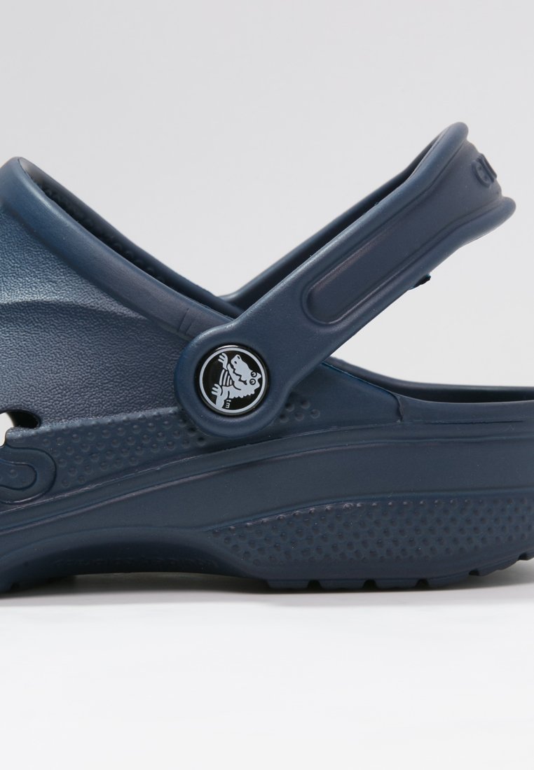 Zoccolo di plastica blu navy con cinturino posteriore, caratterizzato da perforazioni laterali, suola testurizzata e accento con logo circolare.