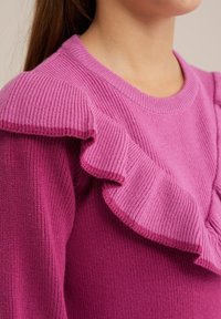 Pink knitted sweater featuring ribbed texture and ruffled accents along the shoulders, with a round neckline and fitted silhouette.