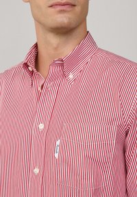 Homme portant une chemise à rayures verticales rouges et blanches avec une poche avant et un col boutonné.