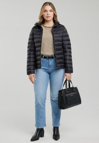 Vrouw draagt een zwarte donsjas, gestreept beige-wit shirt, blauwe spijkerbroek, zwarte riem en laarzen, en houdt een zwarte handtas aan haar zijde vast.