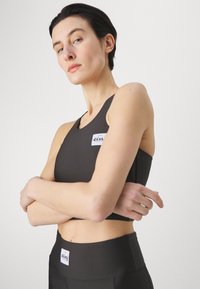 Sutiã desportivo preto e leggings de cintura alta combinando, apresentando um pequeno emblema. O material parece suave e elástico.