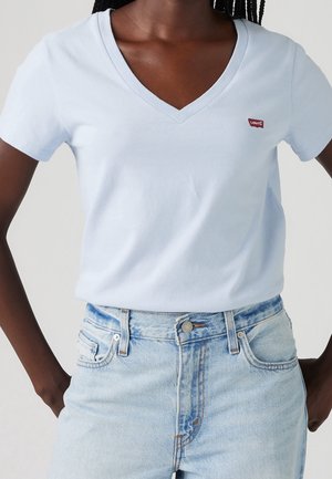 Jasnoniebieska koszulka z dekoltem w serek, wykonana z bawełny. Posiada krótkie rękawy i małe czerwone logo Levi's. Połączona z jasnymi, wysokim stanem dżinsami.