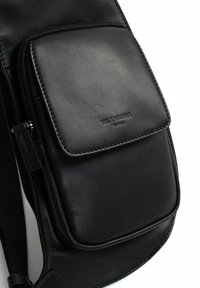 Borsa a tracolla in pelle nera con tasca frontale con zip, texture liscia e branding sottile impresso sul materiale.