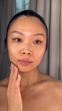 Läheltä kuvattu henkilö, joka levittää ihonhoitotuotetta. Ihossa näkyy sileä ja hehkuva pinta, ja tummanruskea hiukset on kammattu taaksepäin. Paljaat olkapäät ja herkkä kaulaketju ovat näkyvissä.