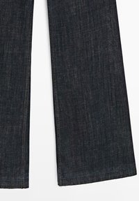 Donkerblauwe denim jeans met rechte pijpen, zichtbare stiksels langs de zijkanten en zomen, plat gelegd op een witte achtergrond.