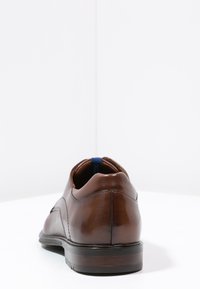 Chaussure habillée en cuir marron avec une finition lisse, un bout arrondi, des coutures discrètes et une semelle profilée basse avec un bord foncé.