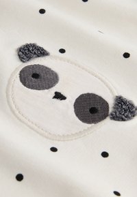 Tela blanca y suave con una cara de panda bordada con orejas y manchas grises, rodeada de pequeños puntos negros.
