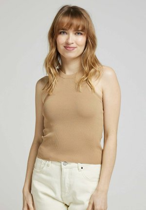 Top sans manches en maille côtelée couleur beige, associé à un jean clair. Texture lisse et design ajusté. Style simple et minimaliste.