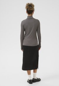 Garā piedurkņu pelēks ribotais turtlenecks, kas kombinēts ar melnu zamša midi svārku ar sānu šķirtni, uzvilkts ar melnām kurpēm un baltām zeķēm.
