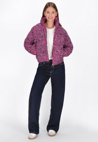 Jachetă puffer roz cu imprimeu leopard negru, guler înalt și fermoare. Asortată cu blugi largi de culoare albastru închis și teniși albi. Cercei în formă de stea.