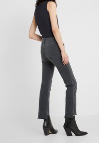 Jeans de mezclilla gris con ajuste slim y dobladillo deshilachado, combinados con botas negras de tobillo. La parte superior es sin mangas y ajustada, en un color oscuro.