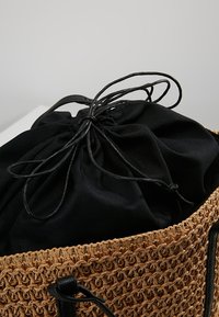 Sac en paille tissé avec une doublure en tissu noir à cordon. Présente des accents en cuir noir et une forme ronde, mettant en avant la texture et le contraste.