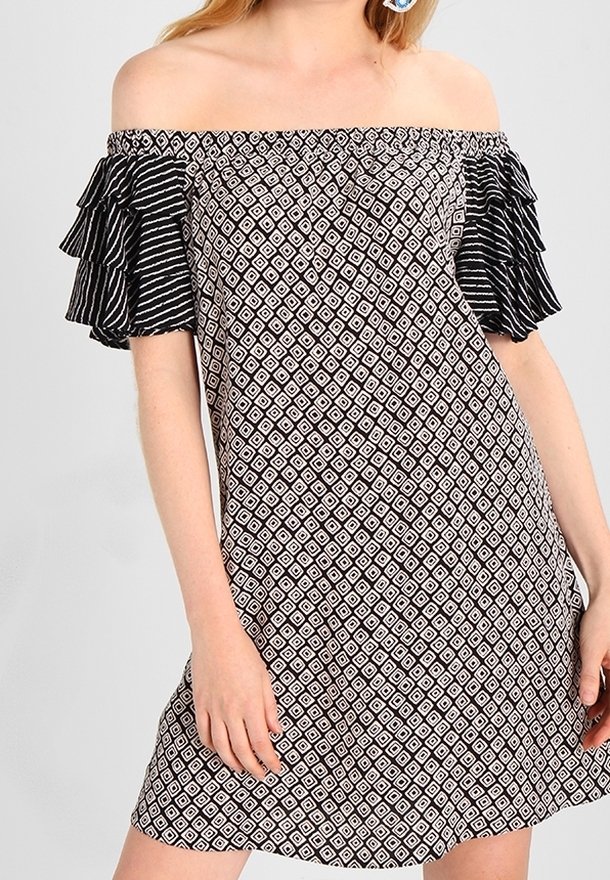 Femme portant une robe épaules dénudées avec un motif losange noir et blanc et des manches courtes rayées à volants.