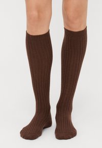 Braune kniek hohe Socken mit geripptem Muster, aus einem weichen Material gefertigt, mit einem engen Sitz am oberen Ende und einer glatten Oberfläche an den Füßen.