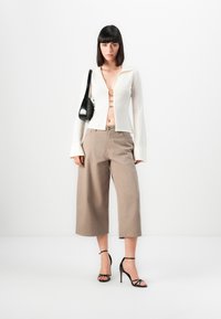 Hvit langermet kort cardigan med krage og frontklips. Kombinert med lysebrune vide bukser og svarte sandaler med stropper.