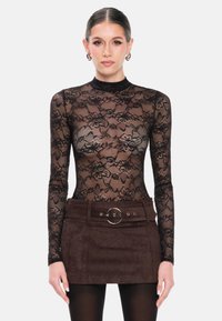 Zwarte kanten bodysuit met bloemmotief, lange mouwen; gecombineerd met een bruine suède rok met een brede riem en een ronde gesp als detail.