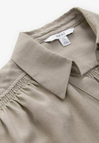 Beige overhemd met kraag van een textuurstof, met gathered details en een label dat aan de binnenkraag is bevestigd.