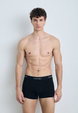 Zwarte katoenen boxershorts met een Calvin Klein-logo op de tailleband, model staat zonder shirt, en toont een slank en getraind lichaam tegen een neutrale achtergrond.