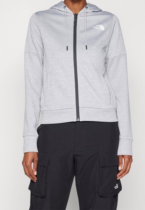 Light grey zip-up hoodie with front pockets and drawstrings, worn with black cargo pants featuring flap pockets.