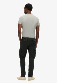 Grijze t-shirt met korte mouwen gecombineerd met zwarte cargo-broek met meerdere zakken, gedragen met beige sneakers. Achteraanzicht, minimalistische achtergrond.