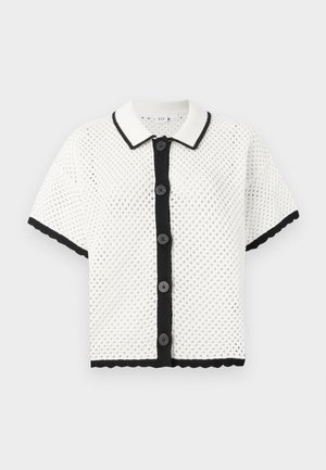 Cardigan en tricot blanc à manches courtes avec une texture perforée, bord noir et six boutons noirs sur le devant. Ourlet festonné accentue les bords.