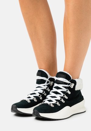 Black suede high-top sneakers with white fur trim and white laces. Features metallic eyelets and a textured, ridged white sole.