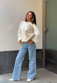 Maglione a maglia crema, jeans a gamba larga blu chiaro e scarpe slip-on bianche perforate. Porta una borsa strutturata beige chiaro.