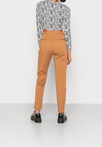 Pantaloni marroni a sigaretta con tasche posteriori, abbinati a una maglia a maniche lunghe bianca e nera con stampa zebra. Scarpe nere stringate completano il look.