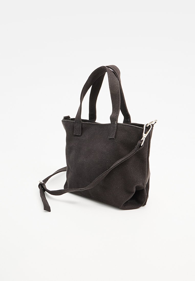Bolso de lona negro con asas cortas y una correa de hombro desmontable, con cierre de cremallera y superficie suave y texturizada.