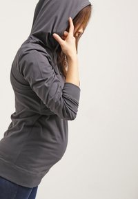 Felpa grigia con cappuccio, dotata di tasca frontale e polsini a costine, design aderente che si adatta intorno alla vita, texture del tessuto morbida.